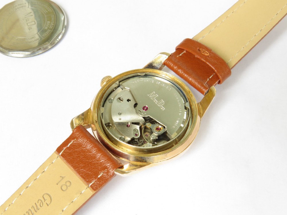 A 1950s gents MuDu Doublematic wristwatch featuring a gold-toned case, cream dial with gold hour markers, date aperture at three oclock, and a brown leather strap. View III