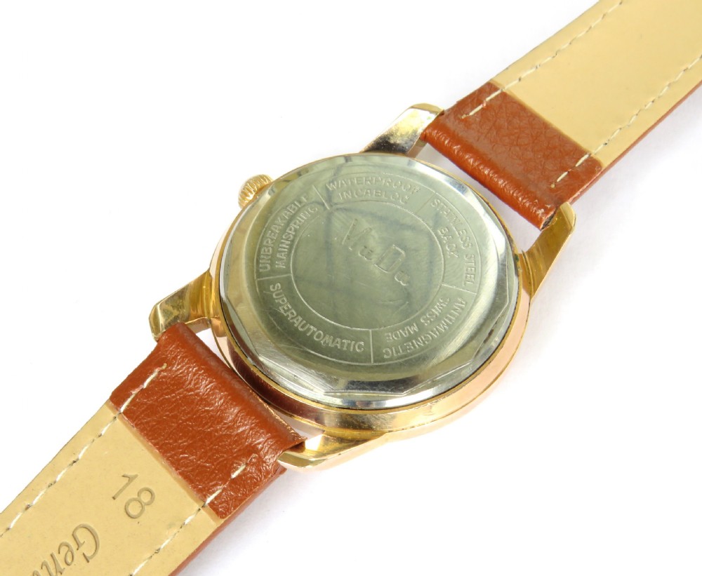 A 1950s gents MuDu Doublematic wristwatch featuring a gold-toned case, cream dial with gold hour markers, date aperture at three oclock, and a brown leather strap. View IV