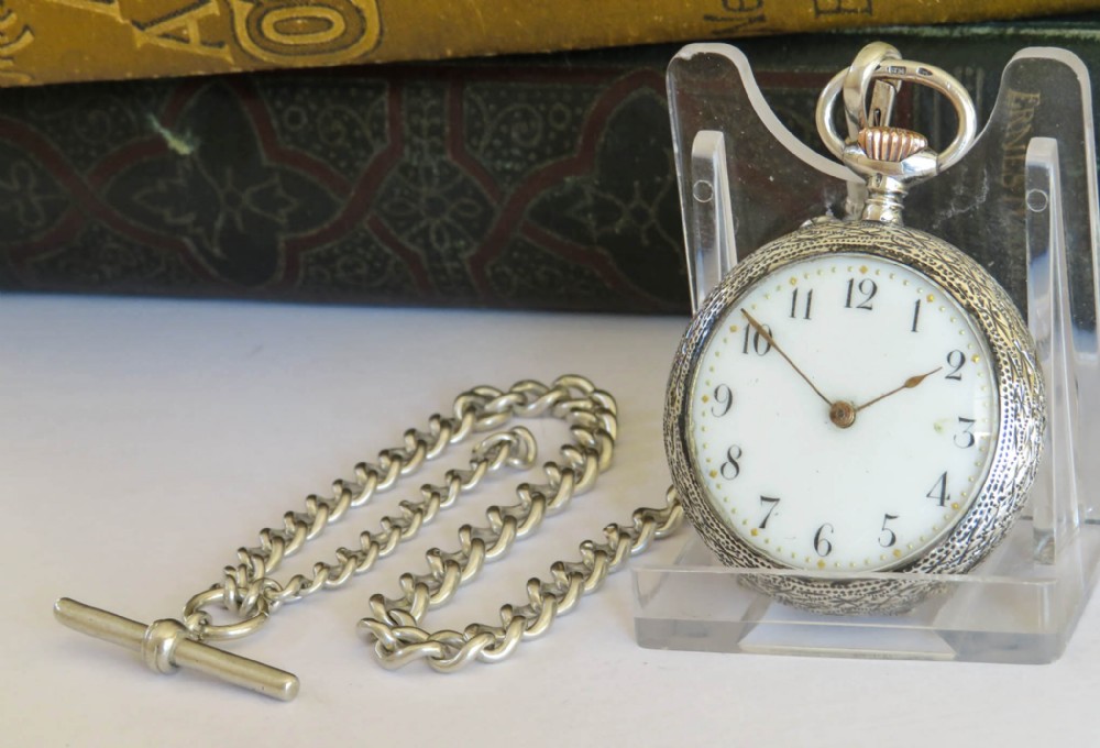 An antique sterling silver fob watch featuring an engraved case and white enamel dial alongside a silver curb-link Albert chain with a T-bar.