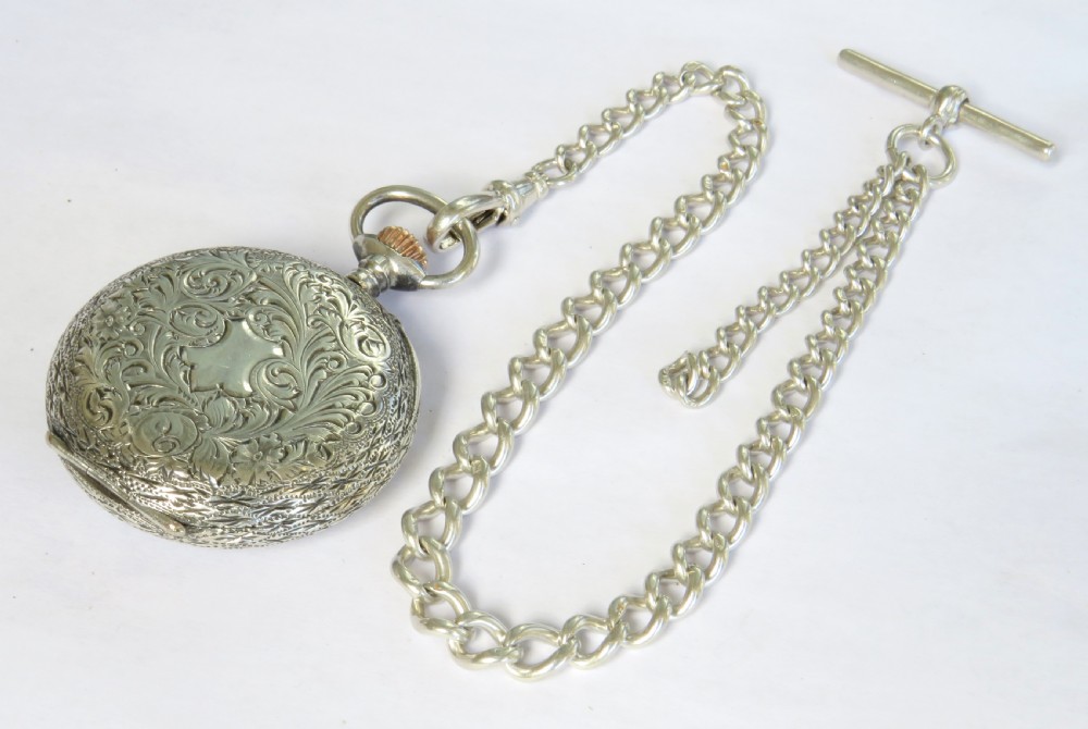 An antique sterling silver fob watch featuring an engraved case and white enamel dial alongside a silver curb-link Albert chain with a T-bar. View VI