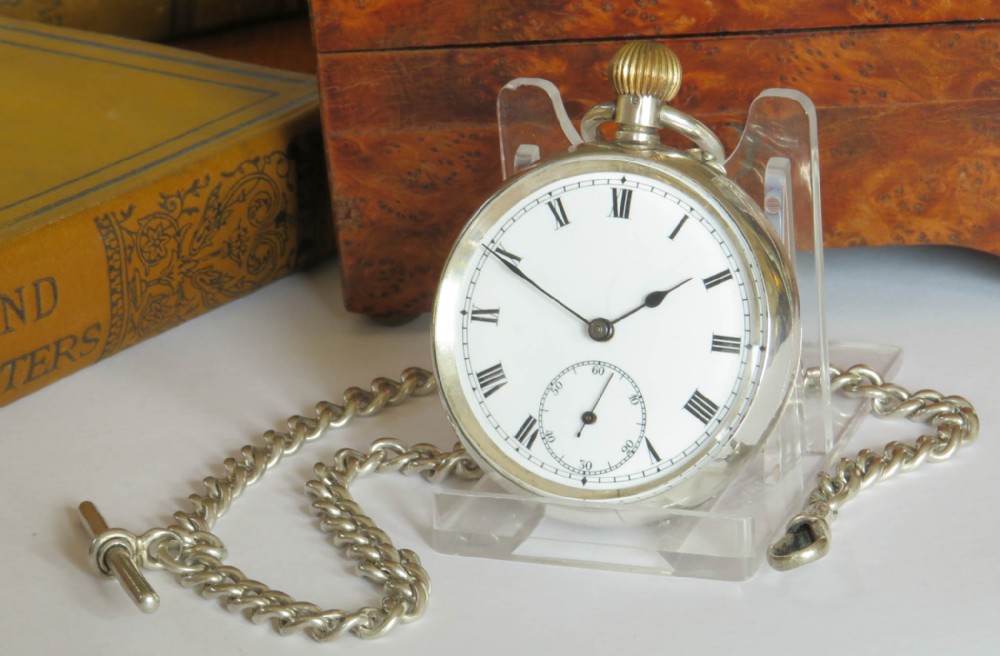 An antique Edwardian open-face silver pocket watch with a white enamel Roman numeral dial and an attached silver T-bar chain.