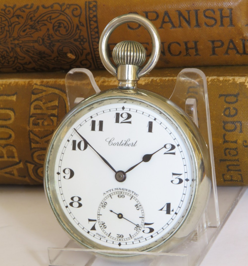 An open-face 1930s Cortebert Swiss pocket watch with a white enamel dial, black Arabic numerals, sub-seconds register, and a polished silver-toned metal case.