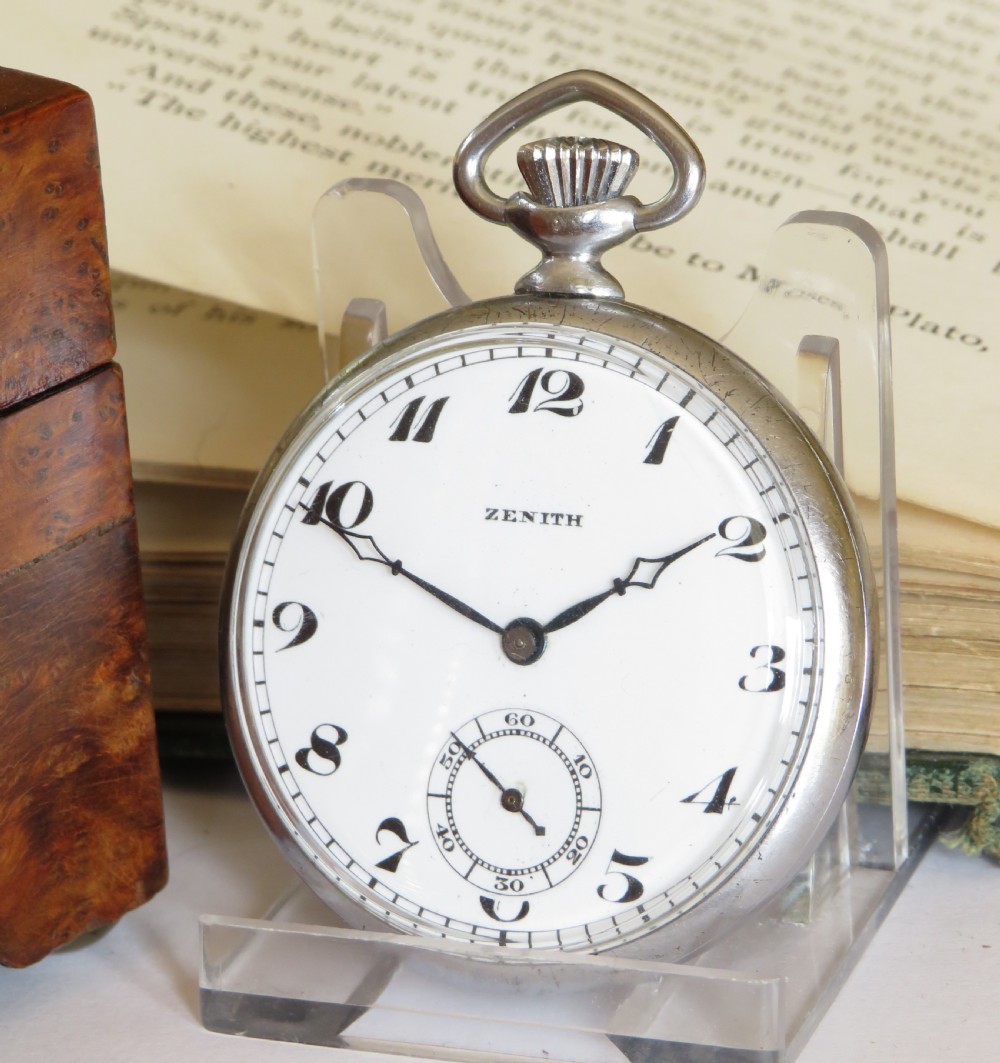 An open-face 1930s Zenith pocket watch featuring a white enamel dial with black Art Deco Arabic numerals, subsidiary seconds dial, and silver-toned metal case.