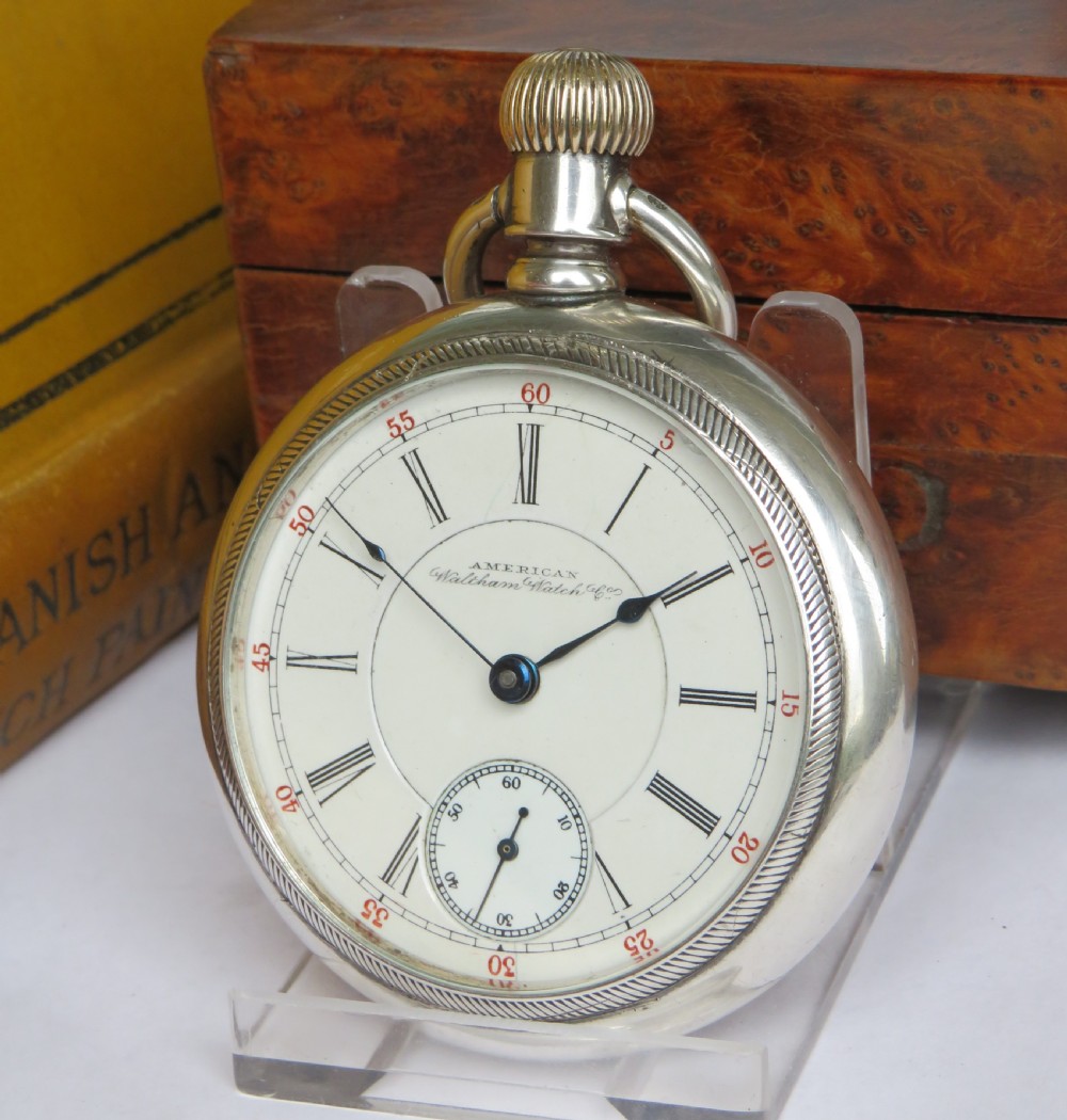 An open-face silver pocket watch featuring a white enamel dial with black Roman numerals, red minute tracking, a subsidiary seconds dial, and blued steel hands.