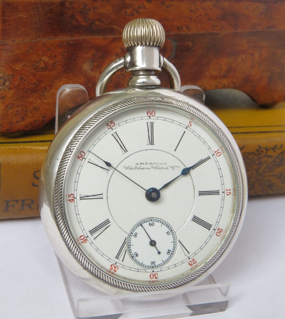 An open-face silver pocket watch featuring a white enamel dial with black Roman numerals, red minute tracking, a subsidiary seconds dial, and blued steel hands. View II