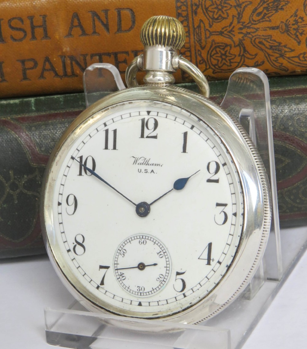 An open-face antique silver pocket watch featuring a white enamel dial, black Arabic numerals, and a subsidiary seconds dial at six oclock.