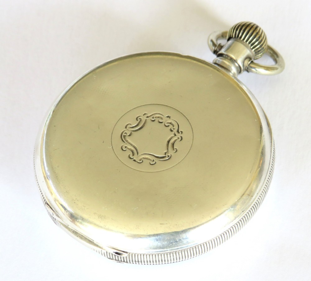 An open-face antique silver pocket watch featuring a white enamel dial, black Arabic numerals, and a subsidiary seconds dial at six oclock. View V