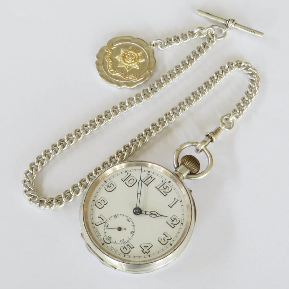 An open-face silver pocket watch with a white enamel dial, black numerals, and sub-seconds dial, attached to a silver curb-link chain with a military badge fob. View III