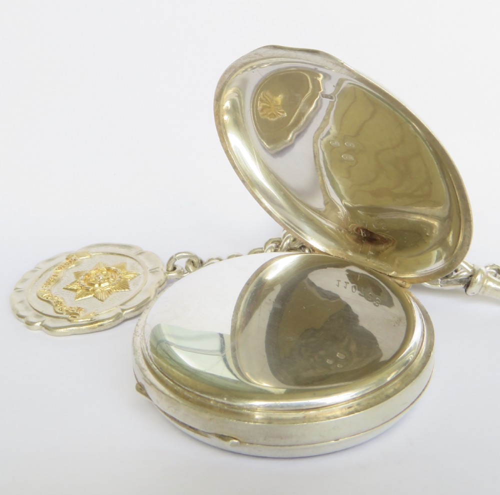 An open-face silver pocket watch with a white enamel dial, black numerals, and sub-seconds dial, attached to a silver curb-link chain with a military badge fob. View IV