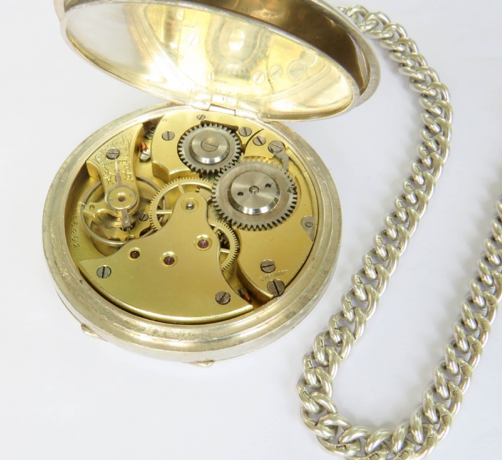 An open-face silver pocket watch with a white enamel dial, black numerals, and sub-seconds dial, attached to a silver curb-link chain with a military badge fob. View V