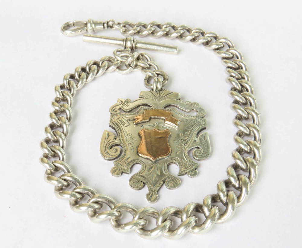 A heavy sterling silver curb link Albert pocket watch chain featuring a T-bar fastener, swivel clip, and an engraved shield fob with rose gold accents.