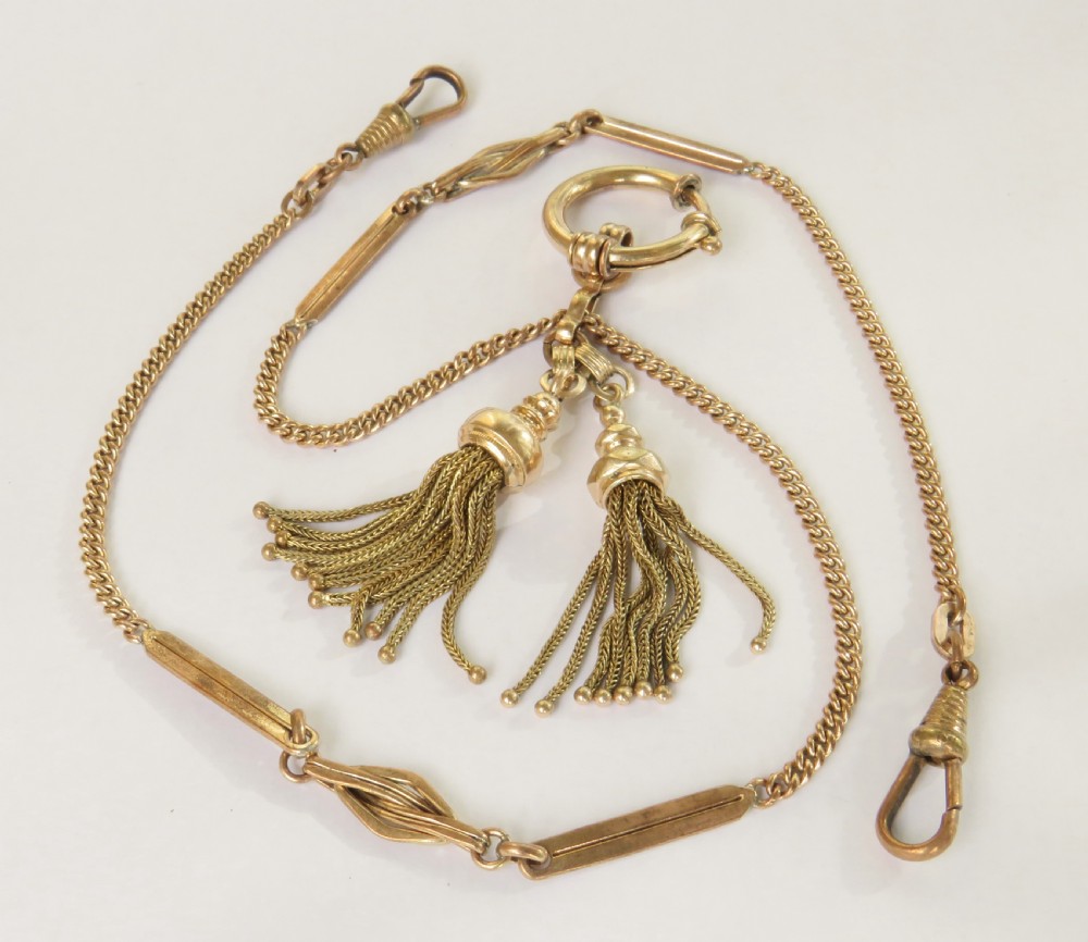 An Edwardian rolled gold double Albert pocket watch chain featuring curb links, decorative bar sections, swivel clasps, a central bolt ring, and two suspended tassels.