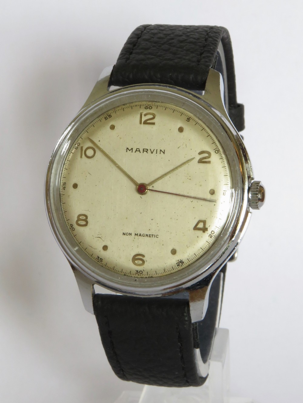 A 1950s gents Marvin wrist watch featuring a cream dial with Arabic numerals, a stainless steel case, and a textured black leather strap.