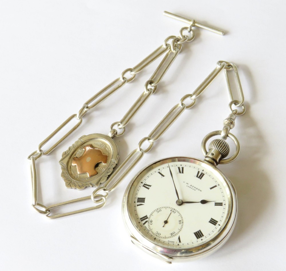 A silver open-face pocket watch displaying black Roman numerals on a white dial, shown alongside a silver chain and decorative fob medallion. View III