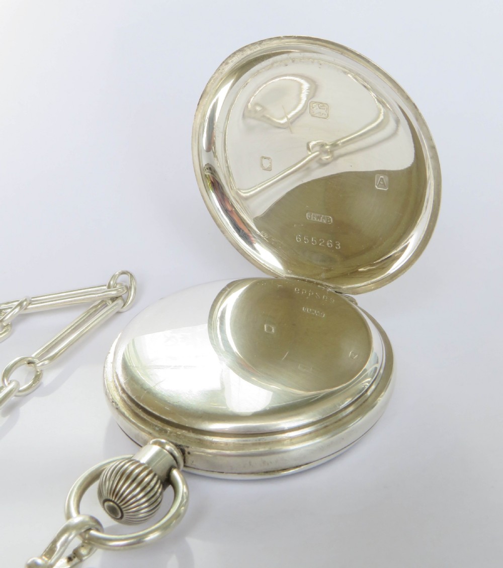 A silver open-face pocket watch displaying black Roman numerals on a white dial, shown alongside a silver chain and decorative fob medallion. View IV
