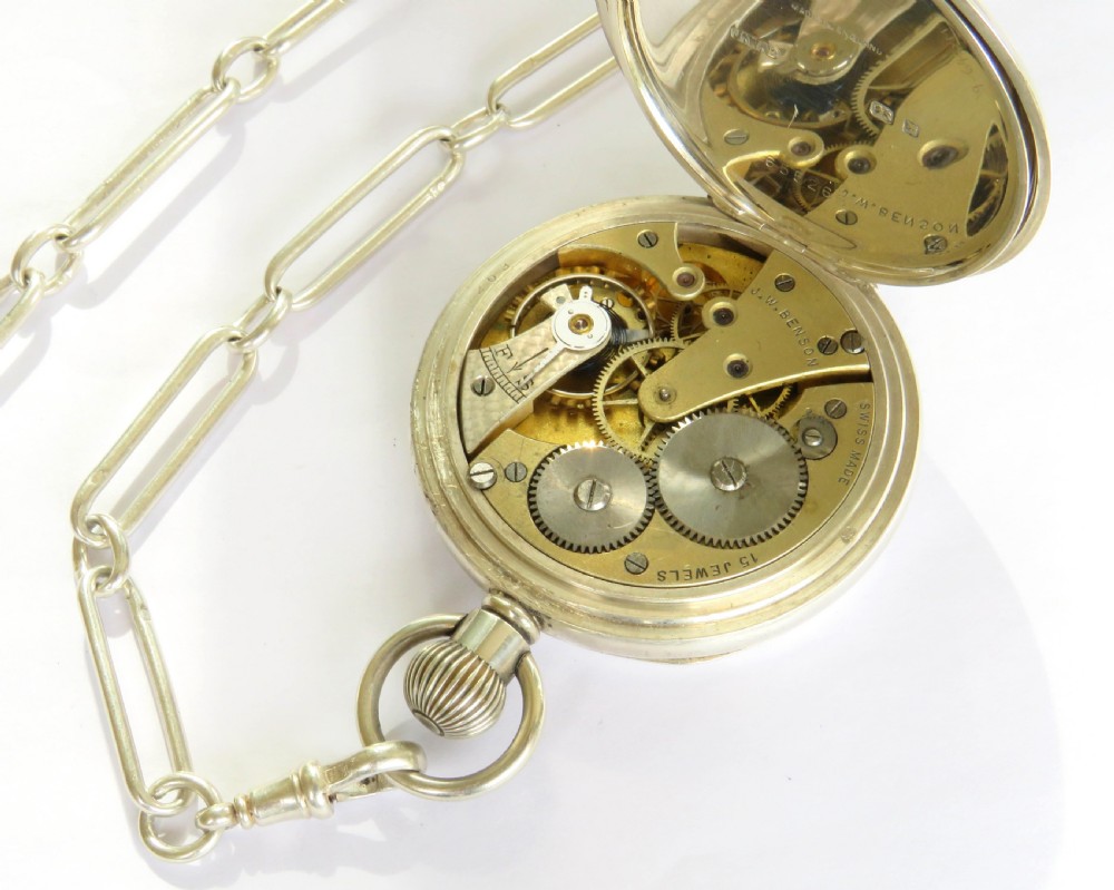 A silver open-face pocket watch displaying black Roman numerals on a white dial, shown alongside a silver chain and decorative fob medallion. View V