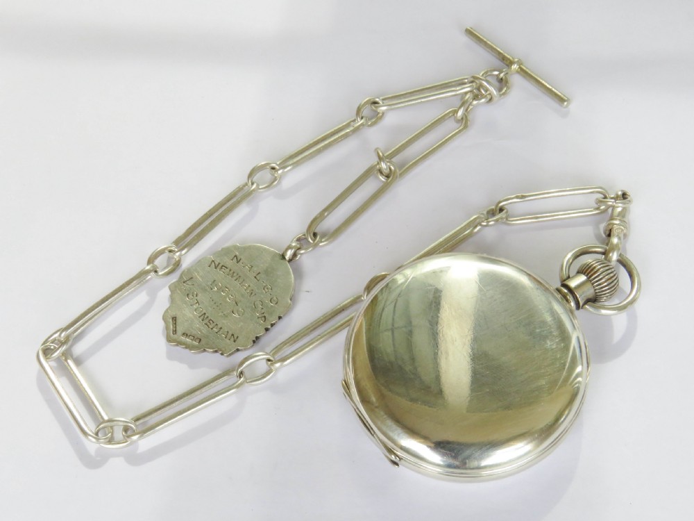A silver open-face pocket watch displaying black Roman numerals on a white dial, shown alongside a silver chain and decorative fob medallion. View VI