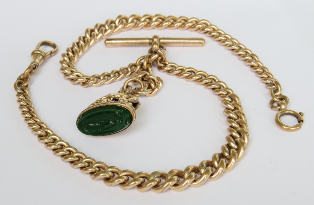 An antique rolled gold curb link Albert watch chain featuring a T-bar, swivel clasp, bolt ring, and a suspended fob with a green oval stone intaglio.