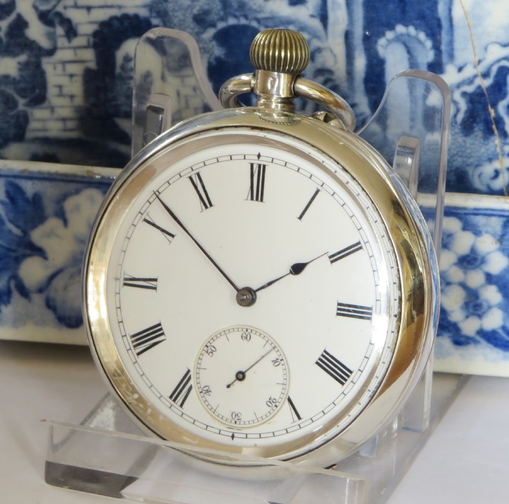 An open-face antique silver pocket watch featuring a white enamel dial with black Roman numerals and a subsidiary seconds dial.