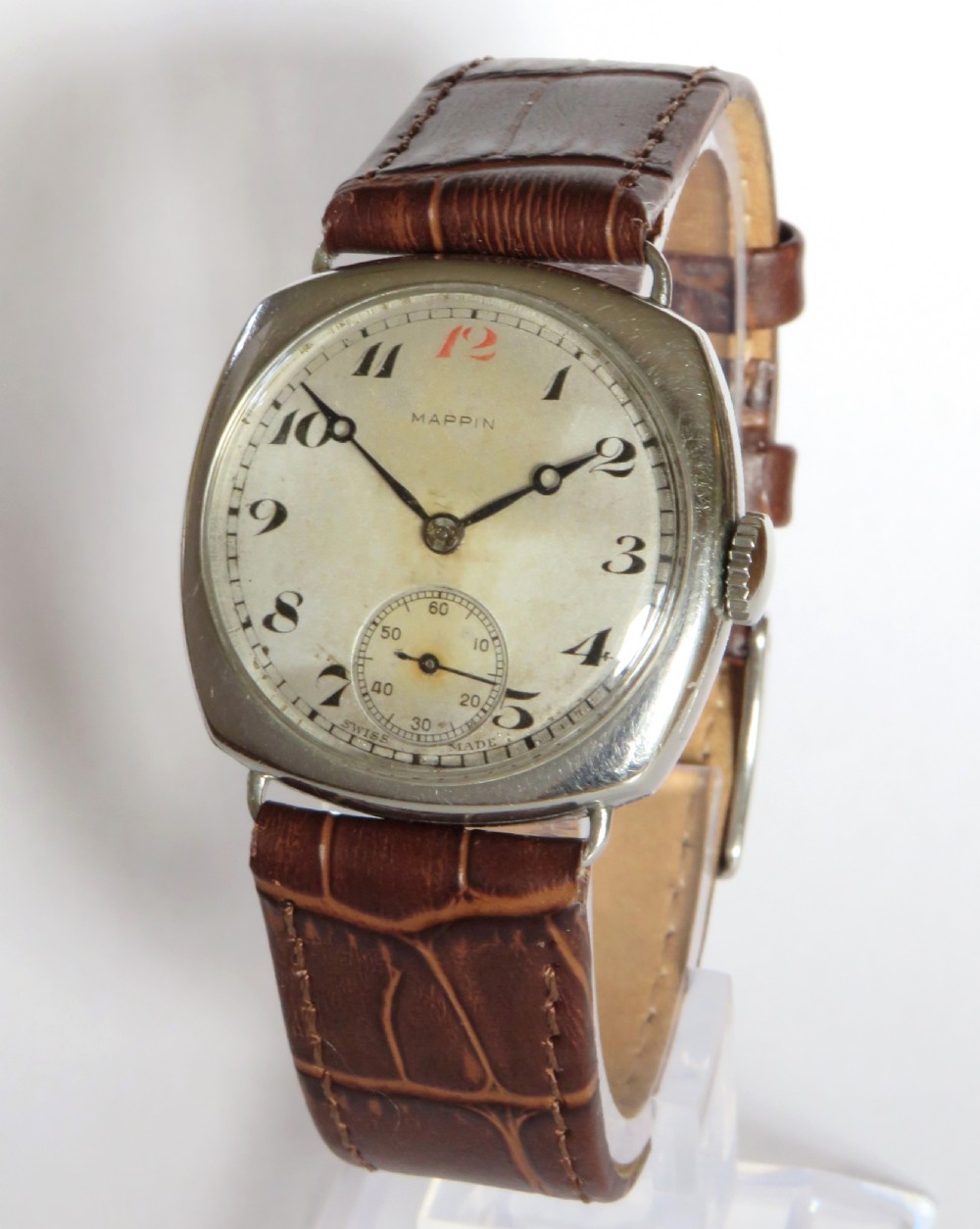 A 1930s cushion-shaped stainless steel wristwatch featuring a light dial with black Arabic numerals, a red twelve marker, a subsidiary seconds dial, and a textured brown leather strap.