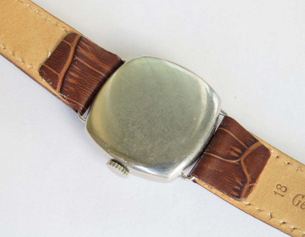 A 1930s cushion-shaped stainless steel wristwatch featuring a light dial with black Arabic numerals, a red twelve marker, a subsidiary seconds dial, and a textured brown leather strap. View IV