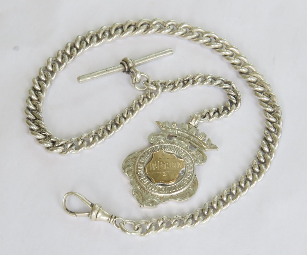 Victorian sterling silver curb link Albert watch chain with a T-bar anchor, swivel clasp, and central crowned shield fob medallion.