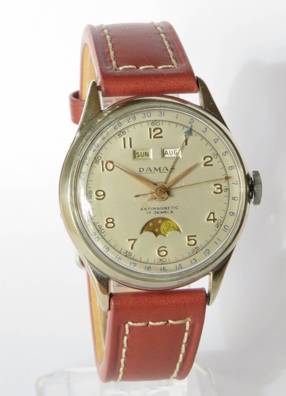 A 1950s Damas gents wrist watch featuring a cream dial with day, month, pointer date, and moonphase complications on a brown leather strap. View II