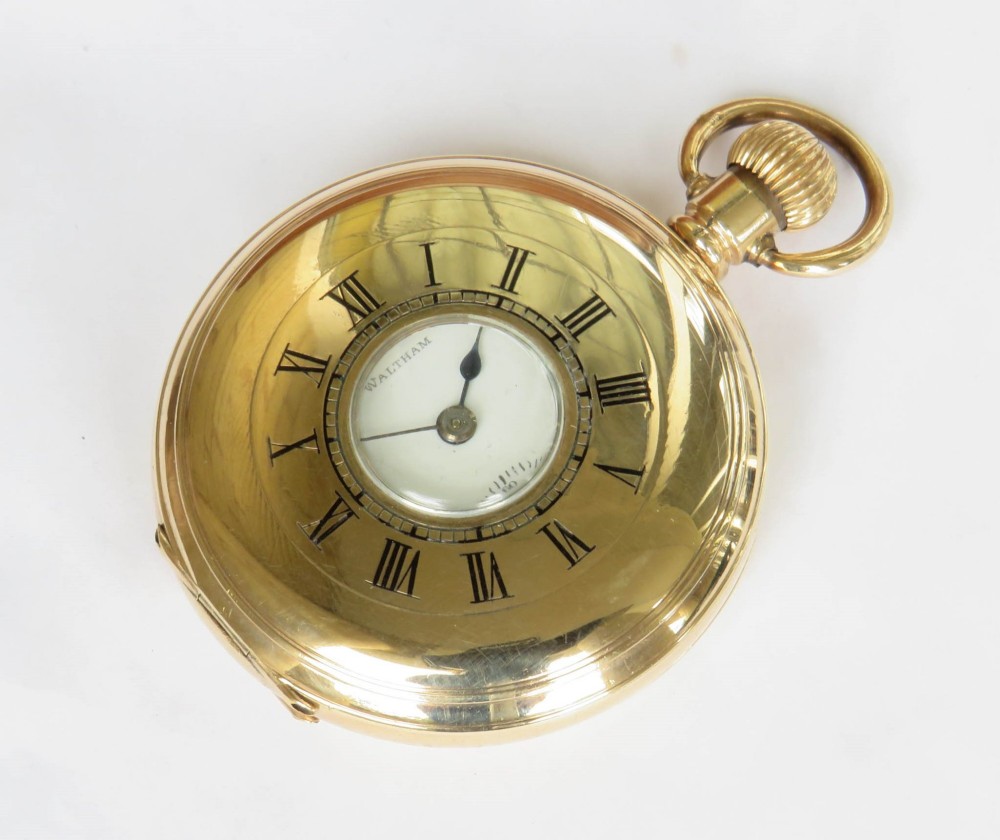 A gold-toned Waltham half hunter pocket watch with Roman numerals engraved around the central circular dial aperture.