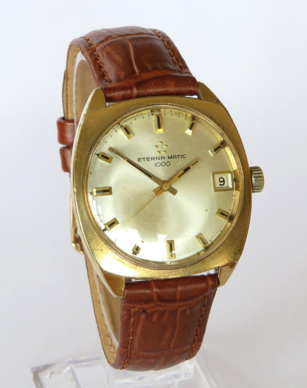 A 1969 gents Eterna-Matic 1000 wristwatch featuring a gold-toned cushion case, champagne dial with date aperture, and brown leather strap. View II