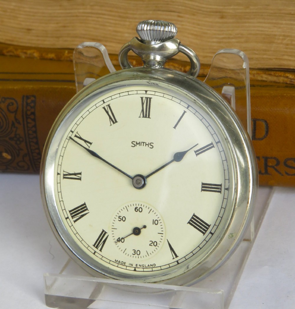 An open-face 1950s Smiths pocket watch featuring a silver-tone chrome case, cream dial with black Roman numerals, and a subsidiary seconds sub-dial.