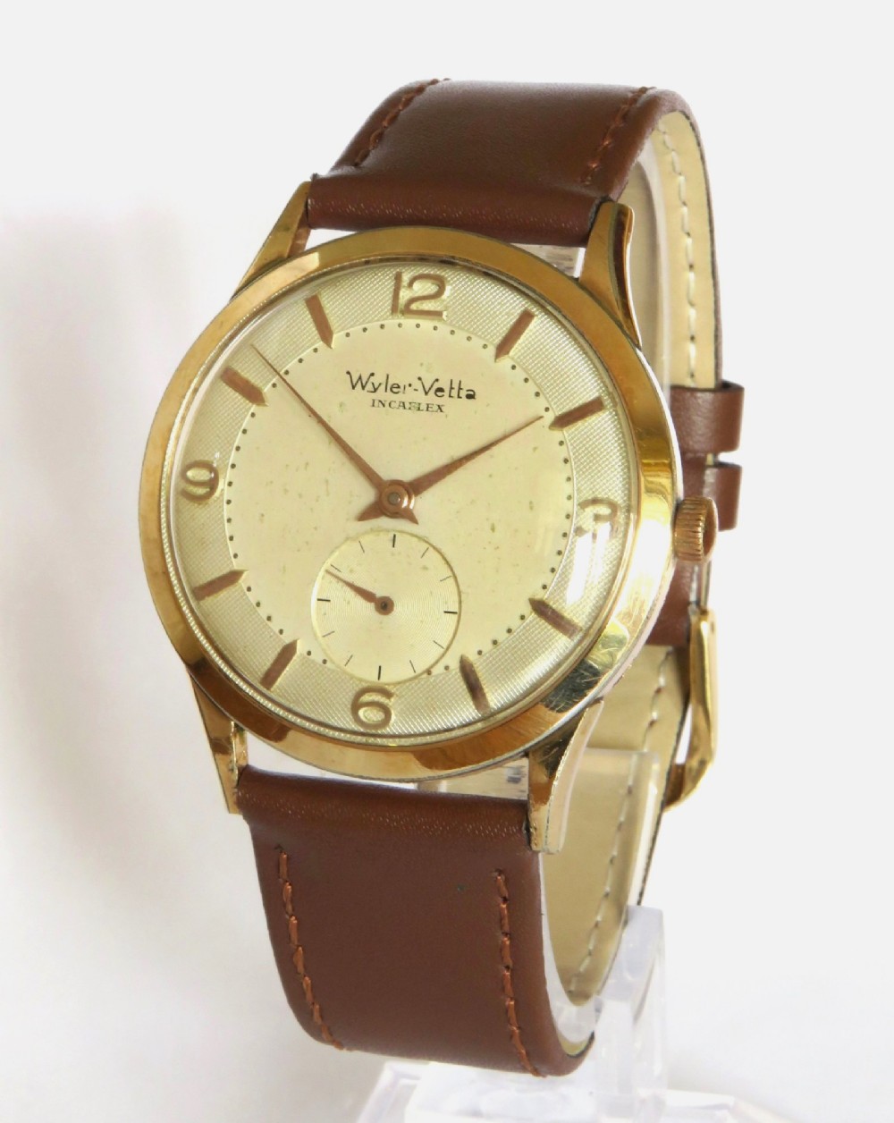 A 1950s Gents Wyler-Vetta wristwatch featuring a gold-toned circular case, cream textured dial with sub-seconds subdial, and a brown leather strap.