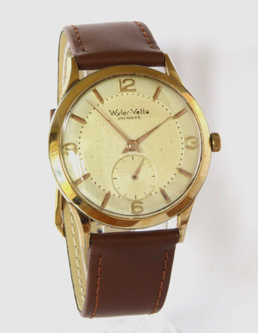 A 1950s Gents Wyler-Vetta wristwatch featuring a gold-toned circular case, cream textured dial with sub-seconds subdial, and a brown leather strap. View II