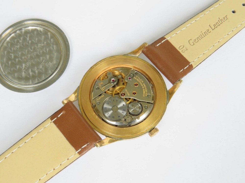 A 1950s Gents Wyler-Vetta wristwatch featuring a gold-toned circular case, cream textured dial with sub-seconds subdial, and a brown leather strap. View V