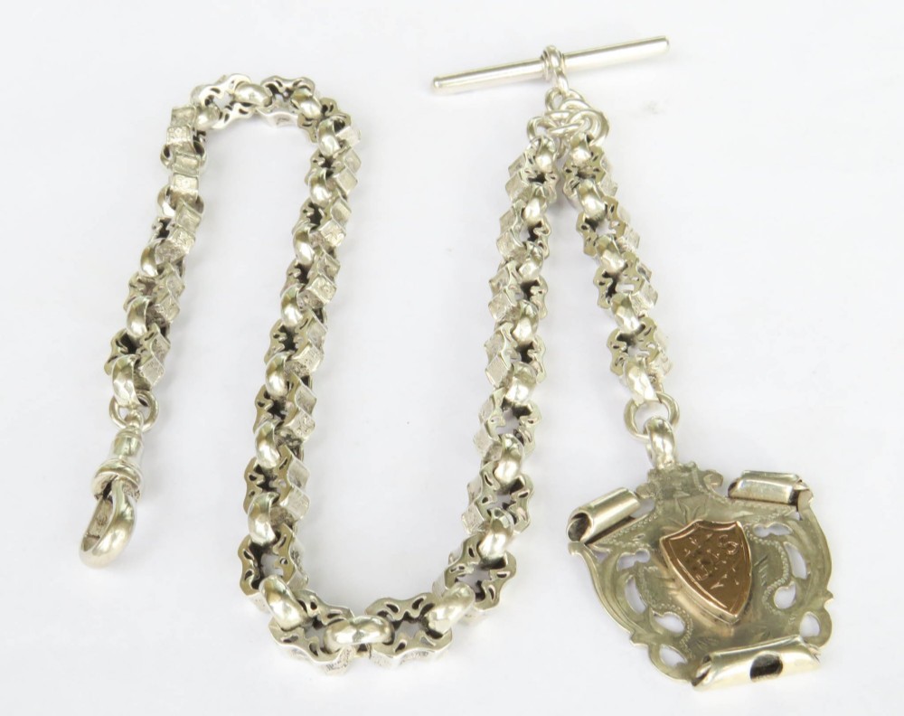 An antique sterling silver pocket watch chain featuring decorative carved links, a T-bar attachment, a swivel clasp, and a shield-shaped fob with gold detailing.
