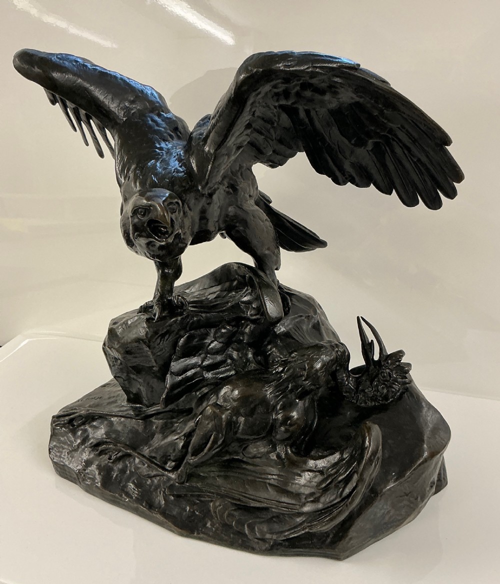 A dark patinated bronze sculpture depicting an eagle with outstretched wings perched on a rocky base above a second bird. View II