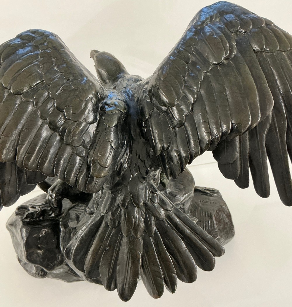 A dark patinated bronze sculpture depicting an eagle with outstretched wings perched on a rocky base above a second bird. View IV