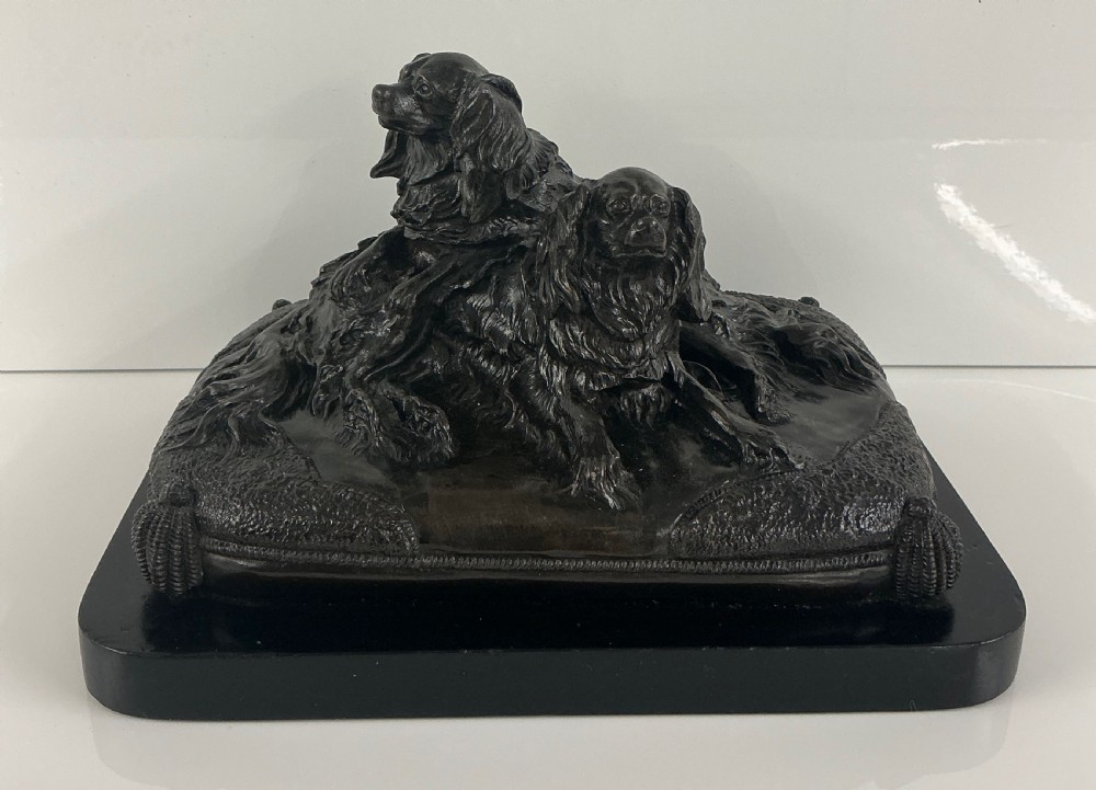 A dark patinated French bronze sculpture depicting two King Charles Spaniels resting on a tasseled cushion mounted on a black base. View II