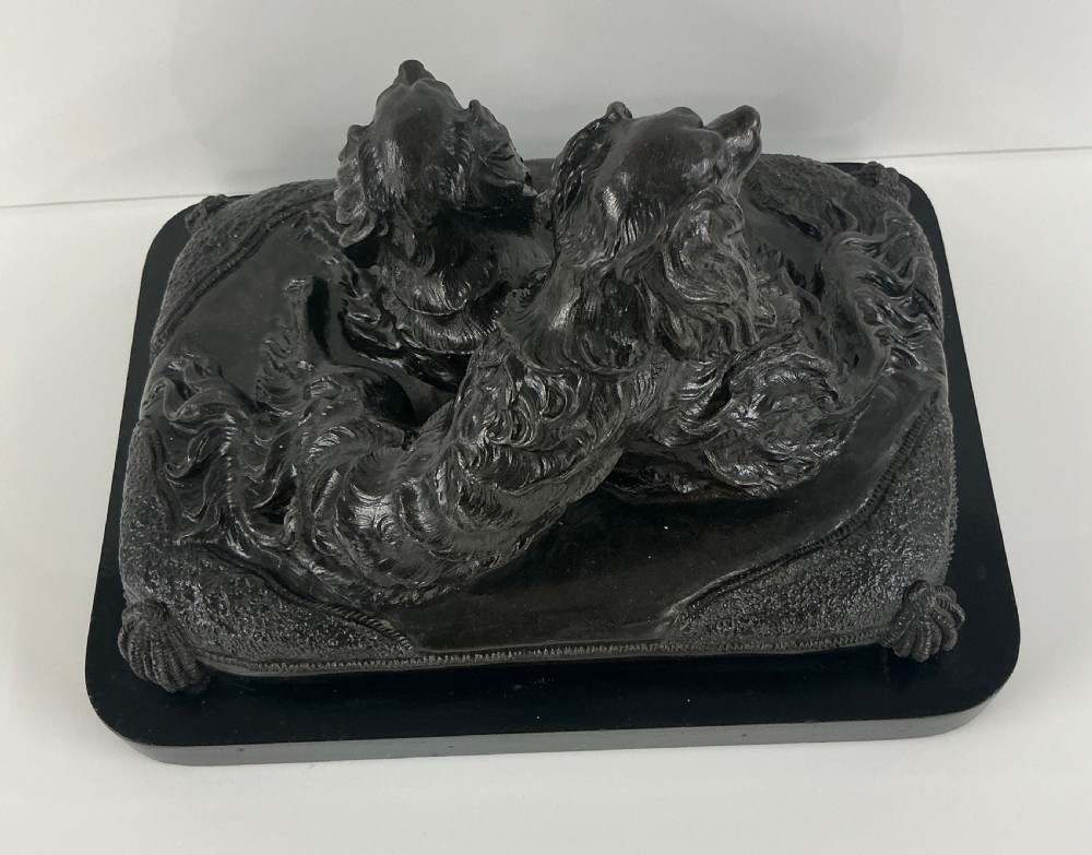 A dark patinated French bronze sculpture depicting two King Charles Spaniels resting on a tasseled cushion mounted on a black base. View III