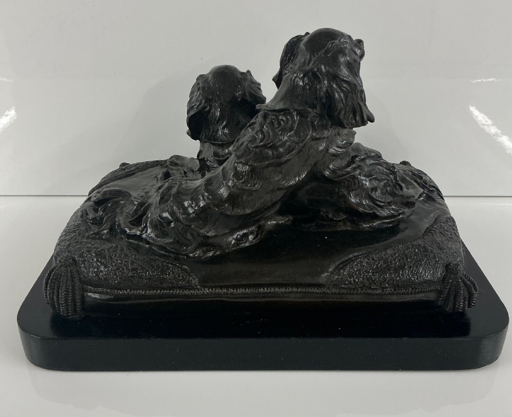 A dark patinated French bronze sculpture depicting two King Charles Spaniels resting on a tasseled cushion mounted on a black base. View IV
