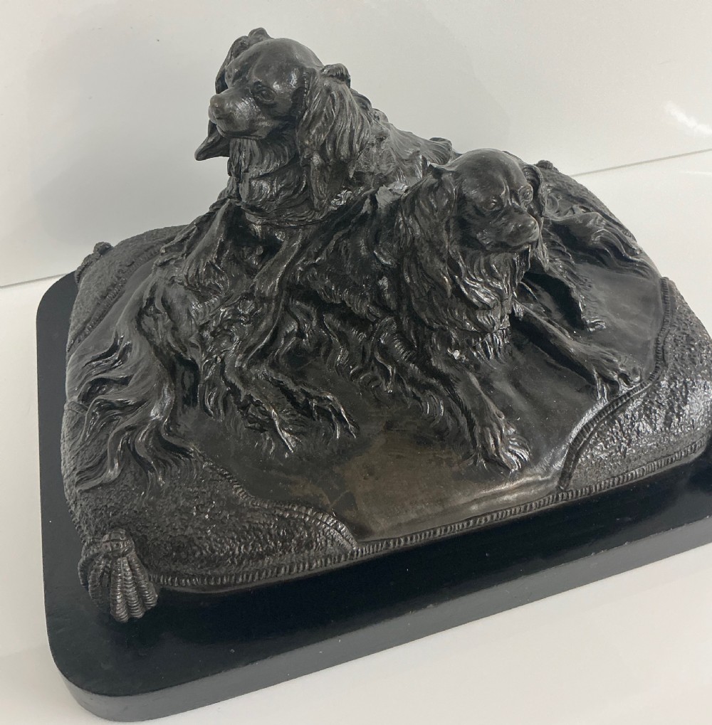 A dark patinated French bronze sculpture depicting two King Charles Spaniels resting on a tasseled cushion mounted on a black base. View V