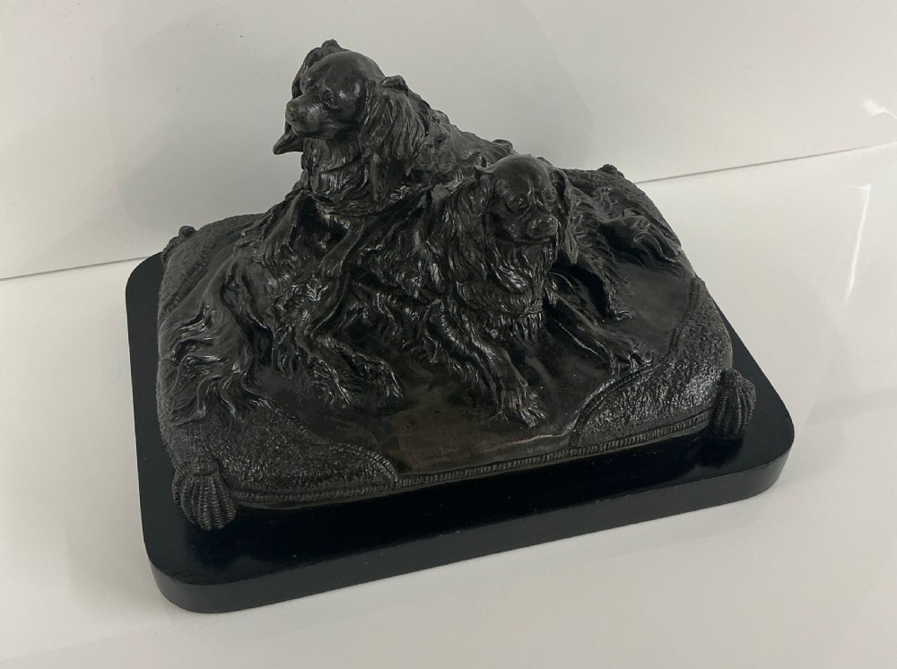 A dark patinated French bronze sculpture depicting two King Charles Spaniels resting on a tasseled cushion mounted on a black base. View VI
