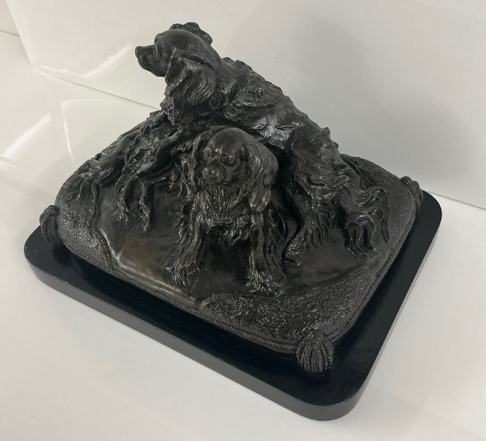 A dark patinated French bronze sculpture depicting two King Charles Spaniels resting on a tasseled cushion mounted on a black base. View VII