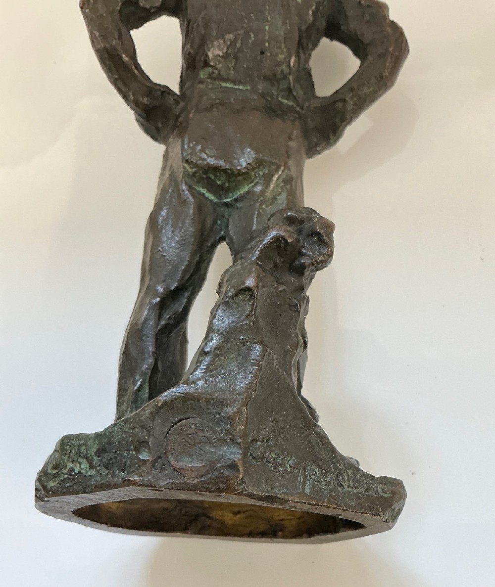 A dark patinated bronze sculpture depicting a standing male worker with his hands resting on his hips. View III
