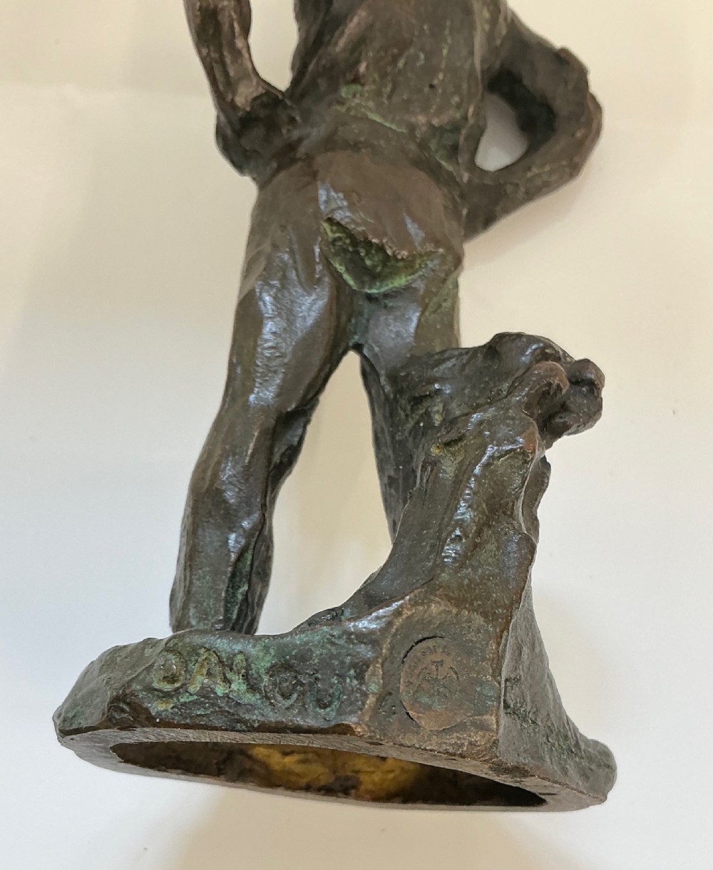 A dark patinated bronze sculpture depicting a standing male worker with his hands resting on his hips. View IV