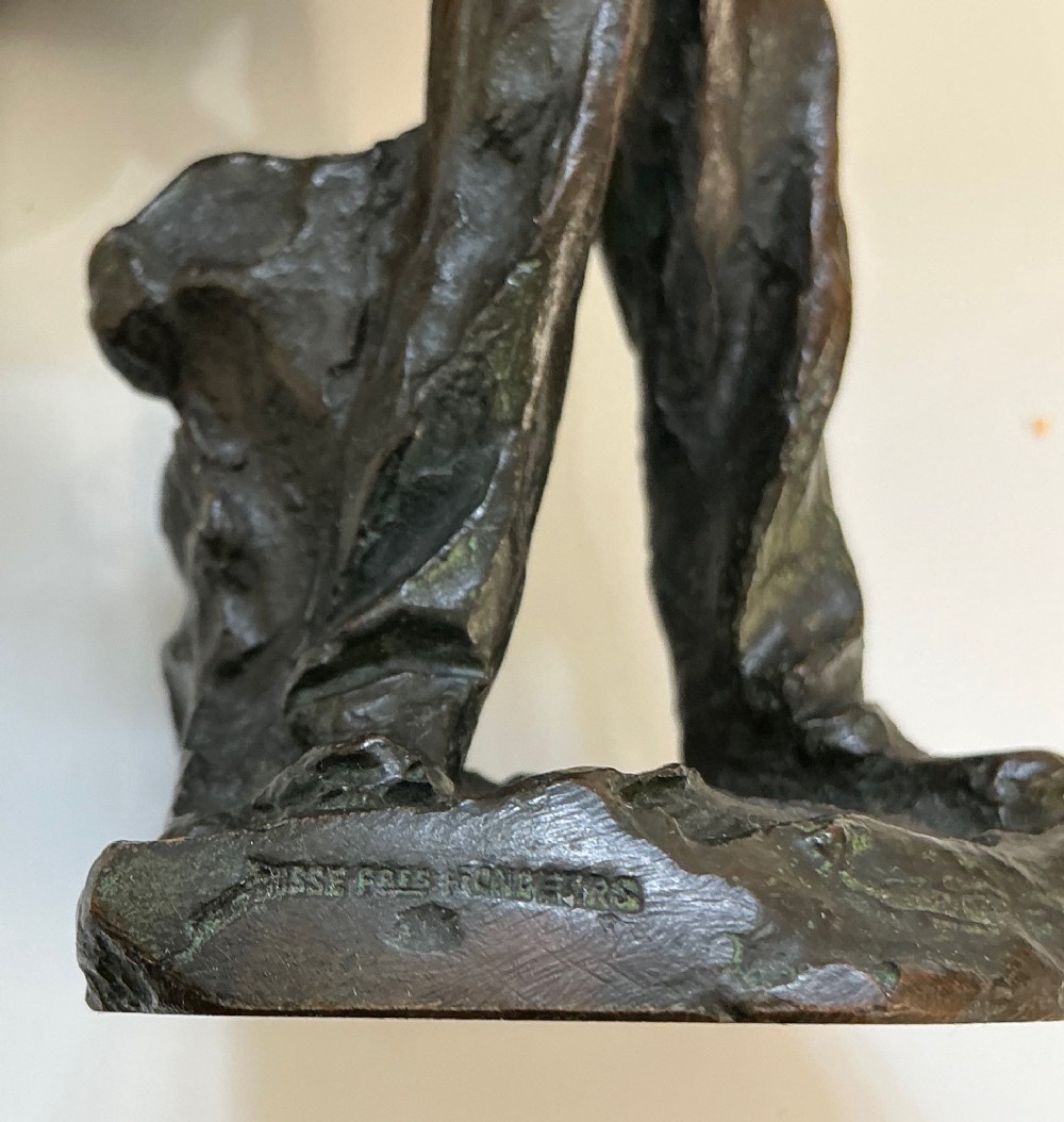 A dark patinated bronze sculpture depicting a standing male worker with his hands resting on his hips. View V