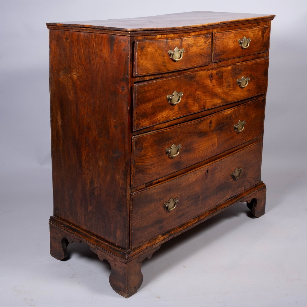 An 18th-century warm brown figured elm chest of drawers featuring a two-over-three drawer configuration with brass handles and shaped bracket feet.
