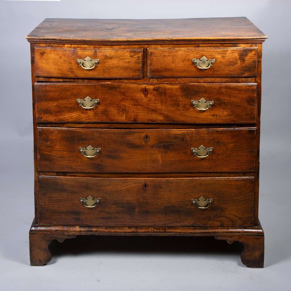An 18th-century warm brown figured elm chest of drawers featuring a two-over-three drawer configuration with brass handles and shaped bracket feet. View II