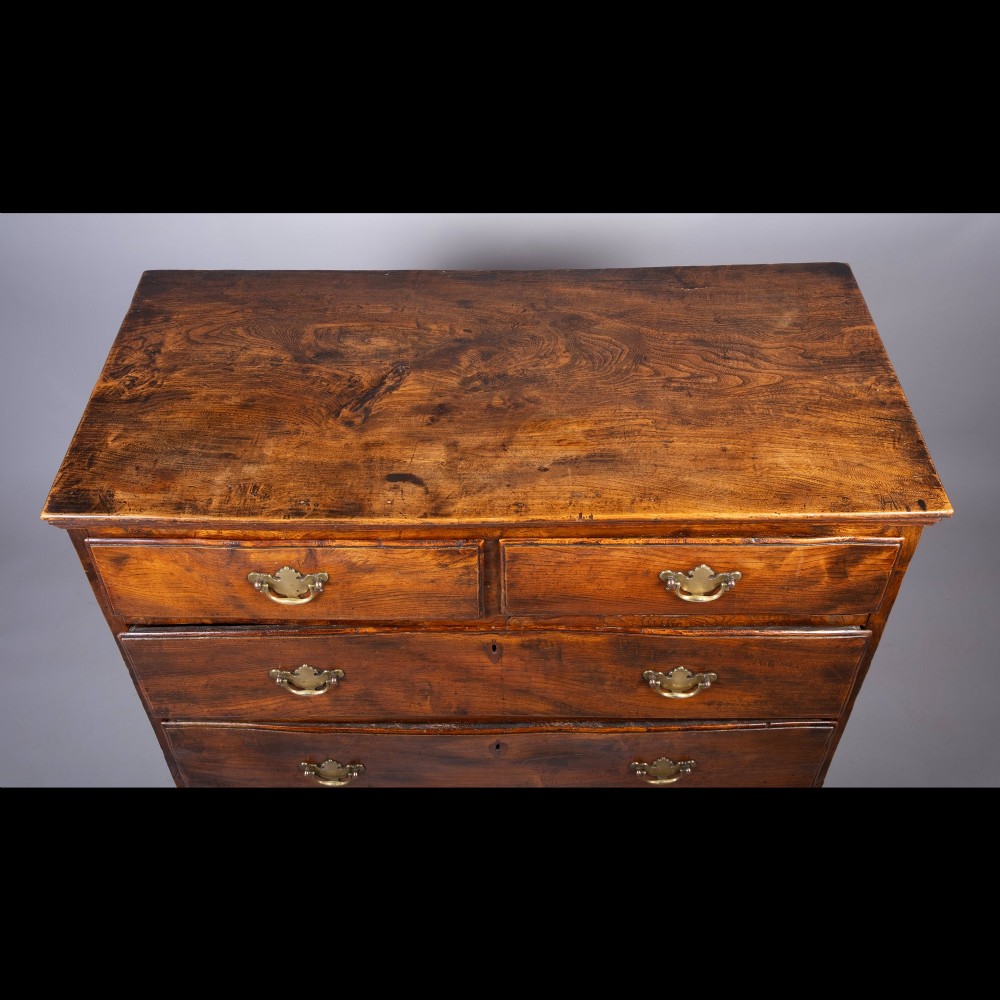 An 18th-century warm brown figured elm chest of drawers featuring a two-over-three drawer configuration with brass handles and shaped bracket feet. View III