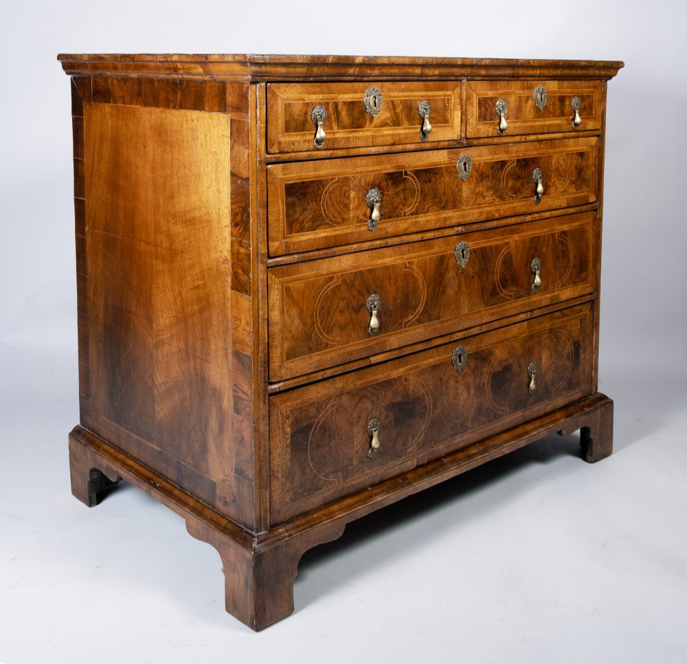 An early 18th-century inlaid walnut chest of drawers featuring two short over three long drawers, brass drop handles, and bracket feet.
