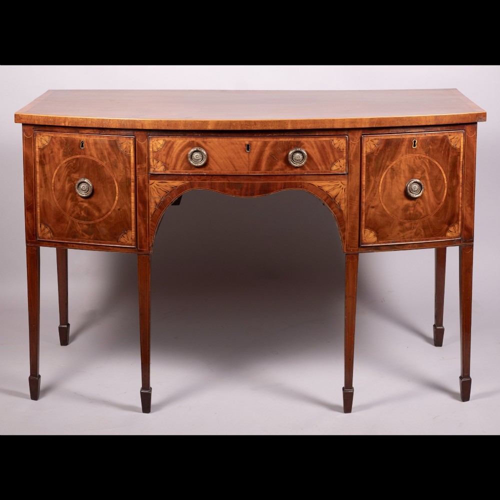 An 18th-century Georgian mahogany bow-fronted sideboard with satinwood inlays, central drawer, two flanking doors, and tapered square legs.